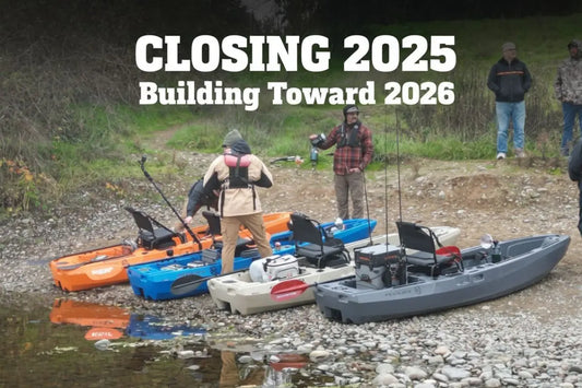 Lineup of FluxJet electric jet fishing kayaks in orange, blue, tan, and grey on the riverbank during end-of-year testing and 2026 production preparations.