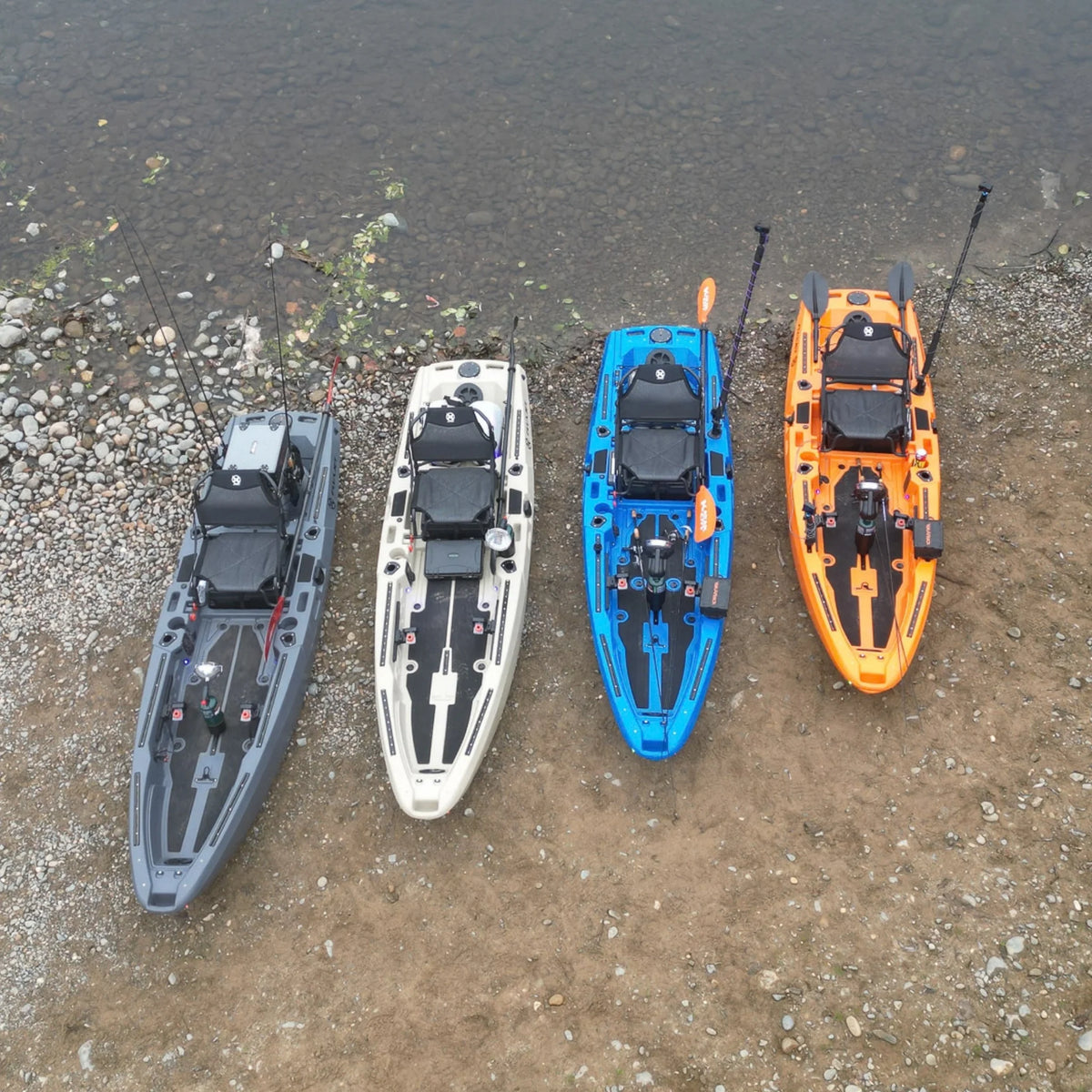 Four FluxJet electric fishing kayaks in gray, tan, blue and orange lined up on the shore