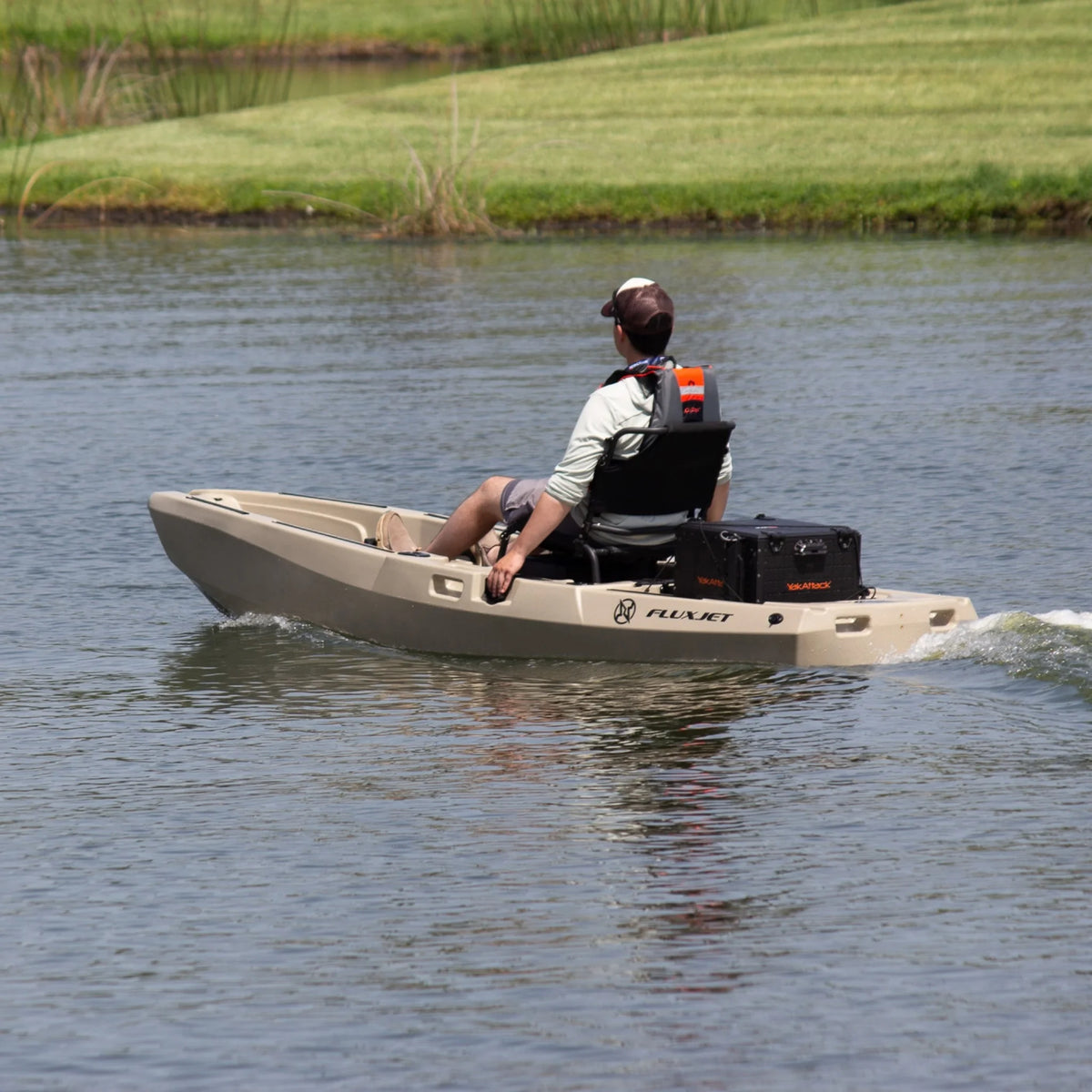 Angler seated on a tan FluxJet electric kayak running on a pond, rear view