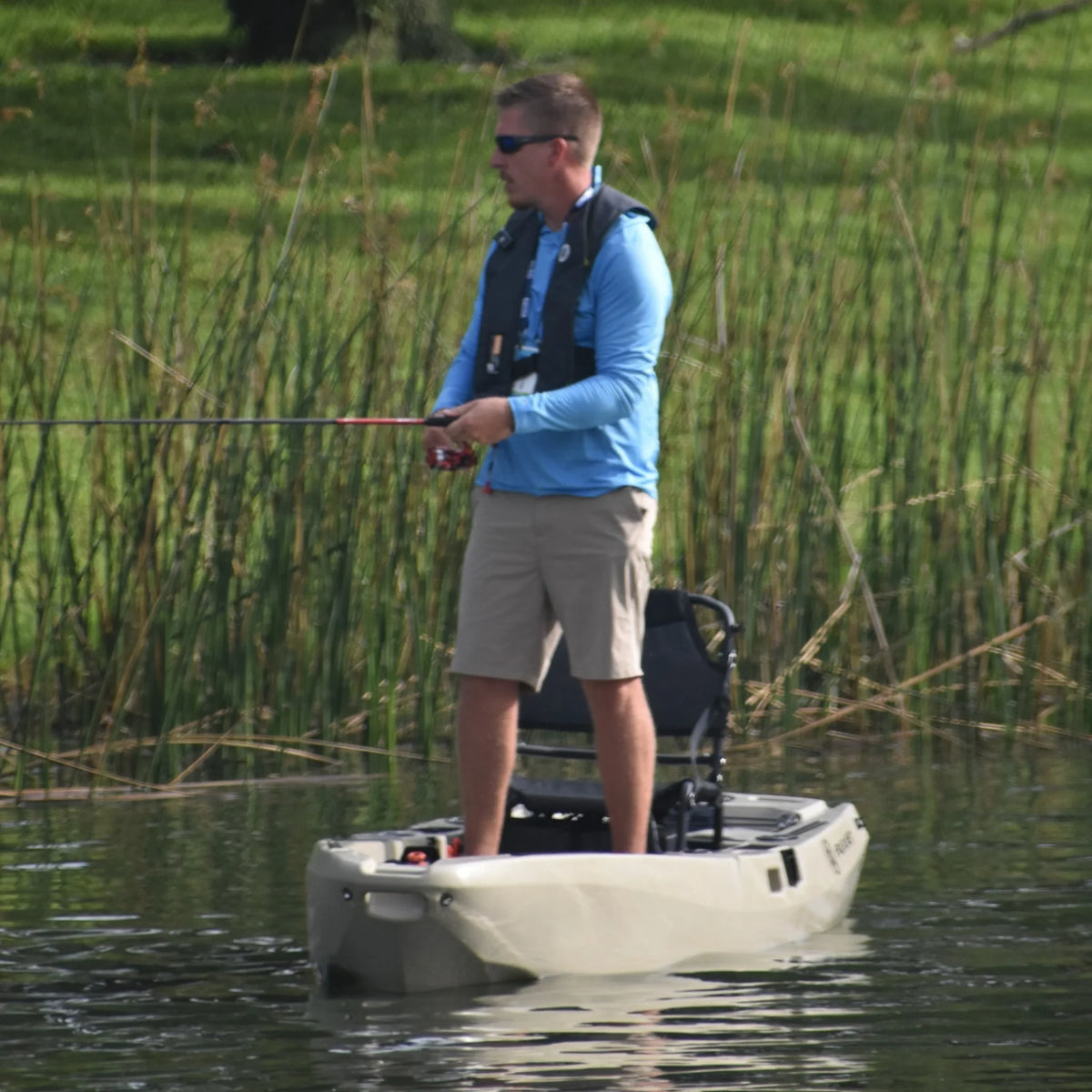 Angler standing and fishing from a tan FluxJet electric kayak near reeds