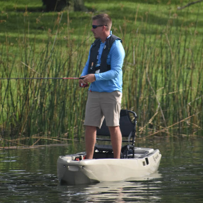 Angler standing and fishing from a tan FluxJet electric kayak near reeds