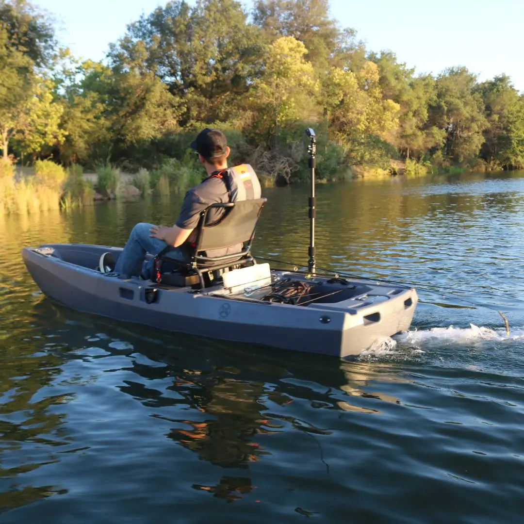 Person fishing from a motorized kayak on a calm lake with trees in the background