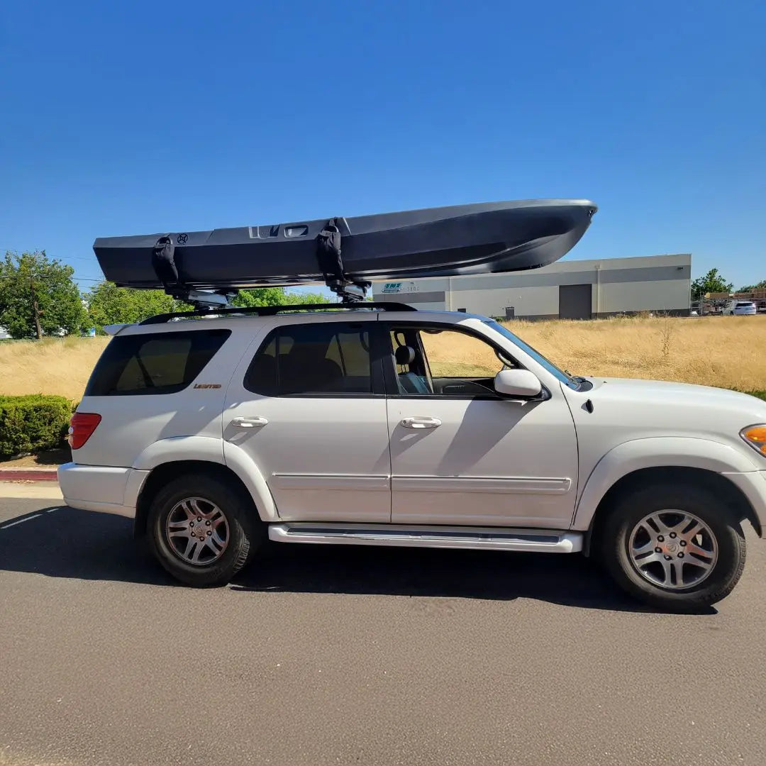 White SUV with a kayak on top parked on a paved surface with a clear blue sky.
