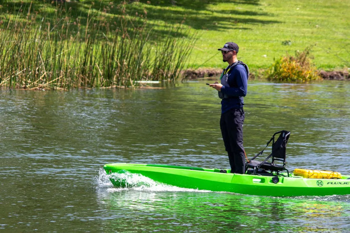 Angler standing upright in a green FluxJet kayak on a lake, showing standing stability