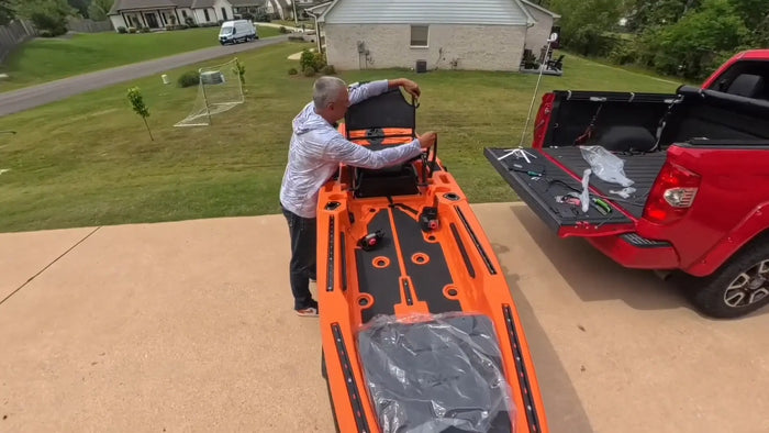 Owner setting up an orange FluxJet kayak in a driveway next to a pickup truck