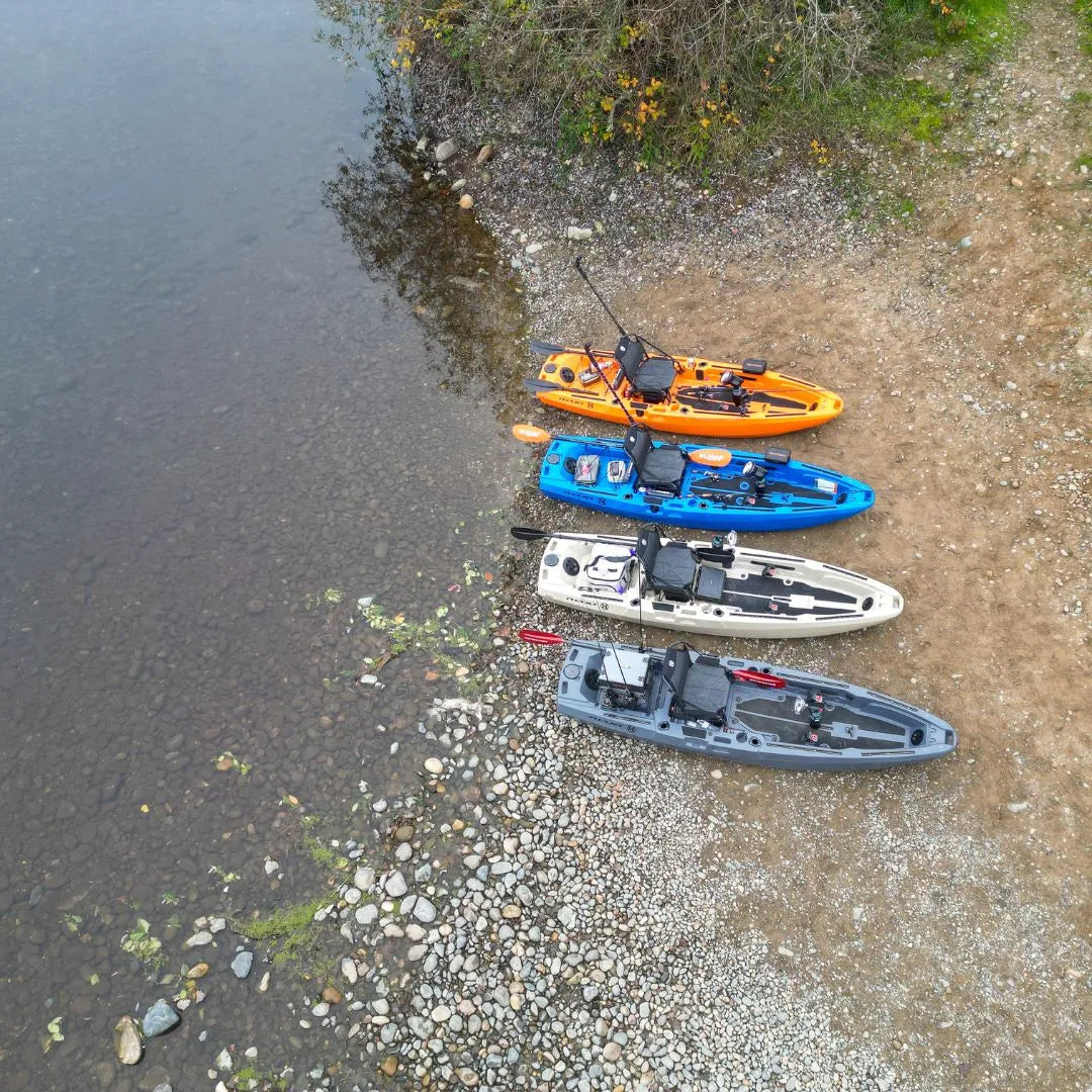  Aerial top-down view of four FluxJet kayaks stacked in a line on a rocky riverbank beside shallow water.