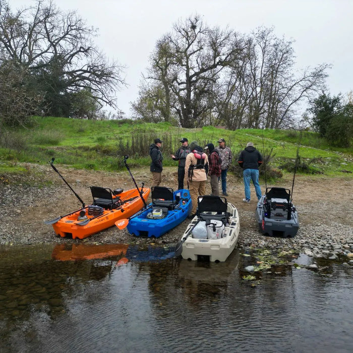 Group of anglers talking beside several FluxJet kayaks lined up on a rocky riverbank during a demo day