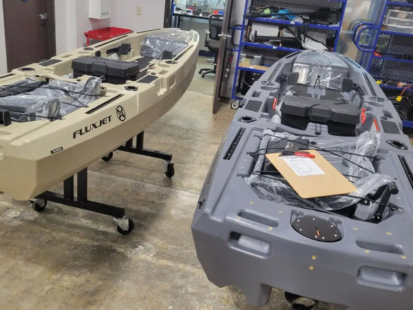 Tan and gray FluxJet kayaks on stands being prepared in the warehouse