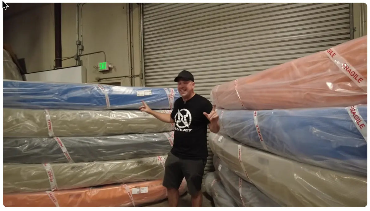 Jason from FluxJet standing between stacks of wrapped FluxJet kayak hulls at the Sacramento factory